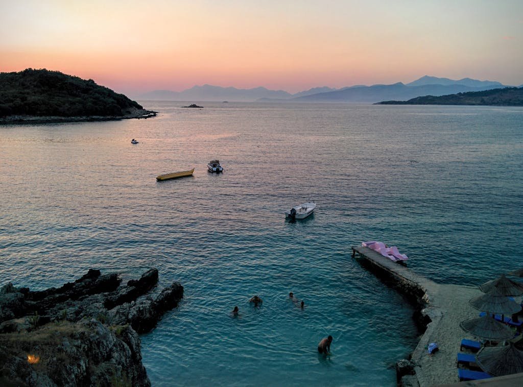 Golden sunset over Ksamil beach with swimmers and boats in a tranquil seascape.