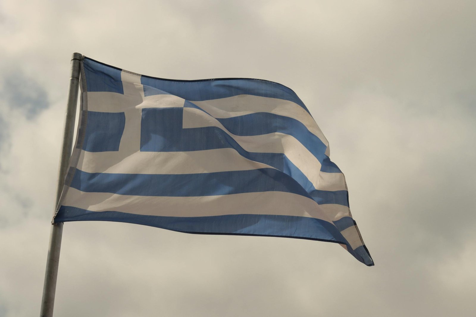 A Greek flag waving proudly against a cloudy sky in Athens, Greece.